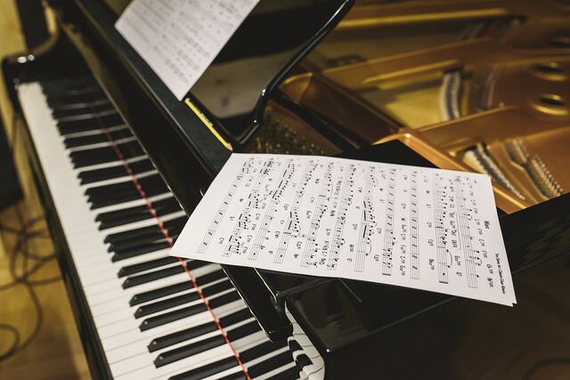 Handwritten music manuscript pages lying on the music rest of a grand piano, the strings and gold frame visible under the raised lid.